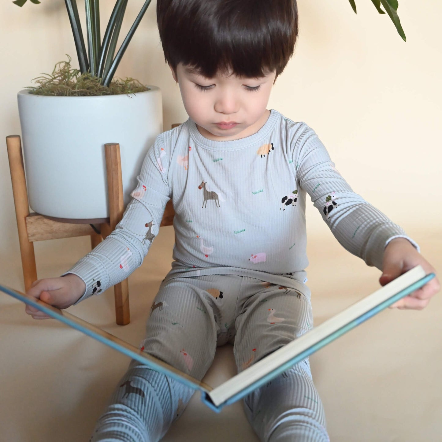 toddler boy in farm animal pattern pajamas reading a board book