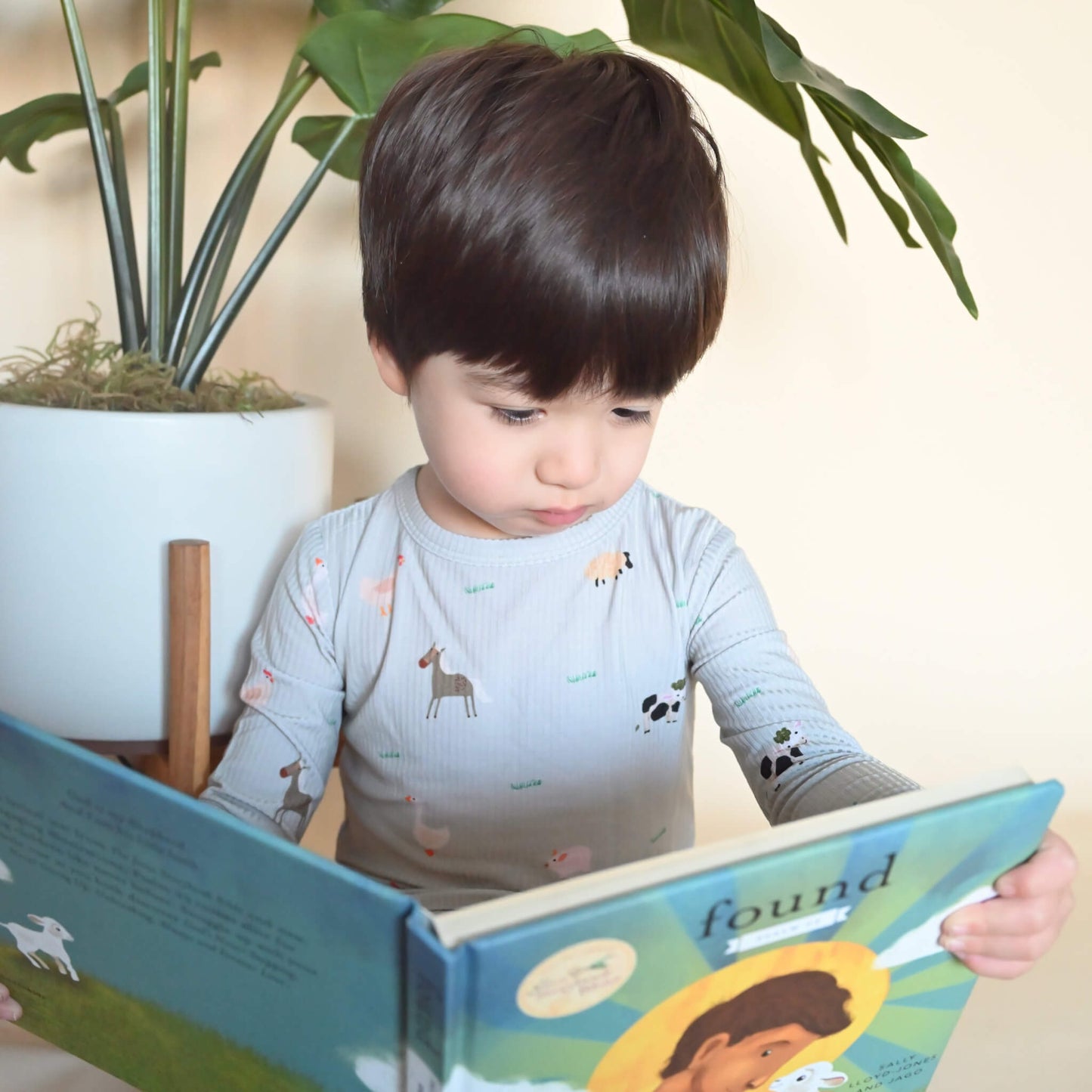 toddler boy in farm animal pattern pajamas reading Christian kid's book