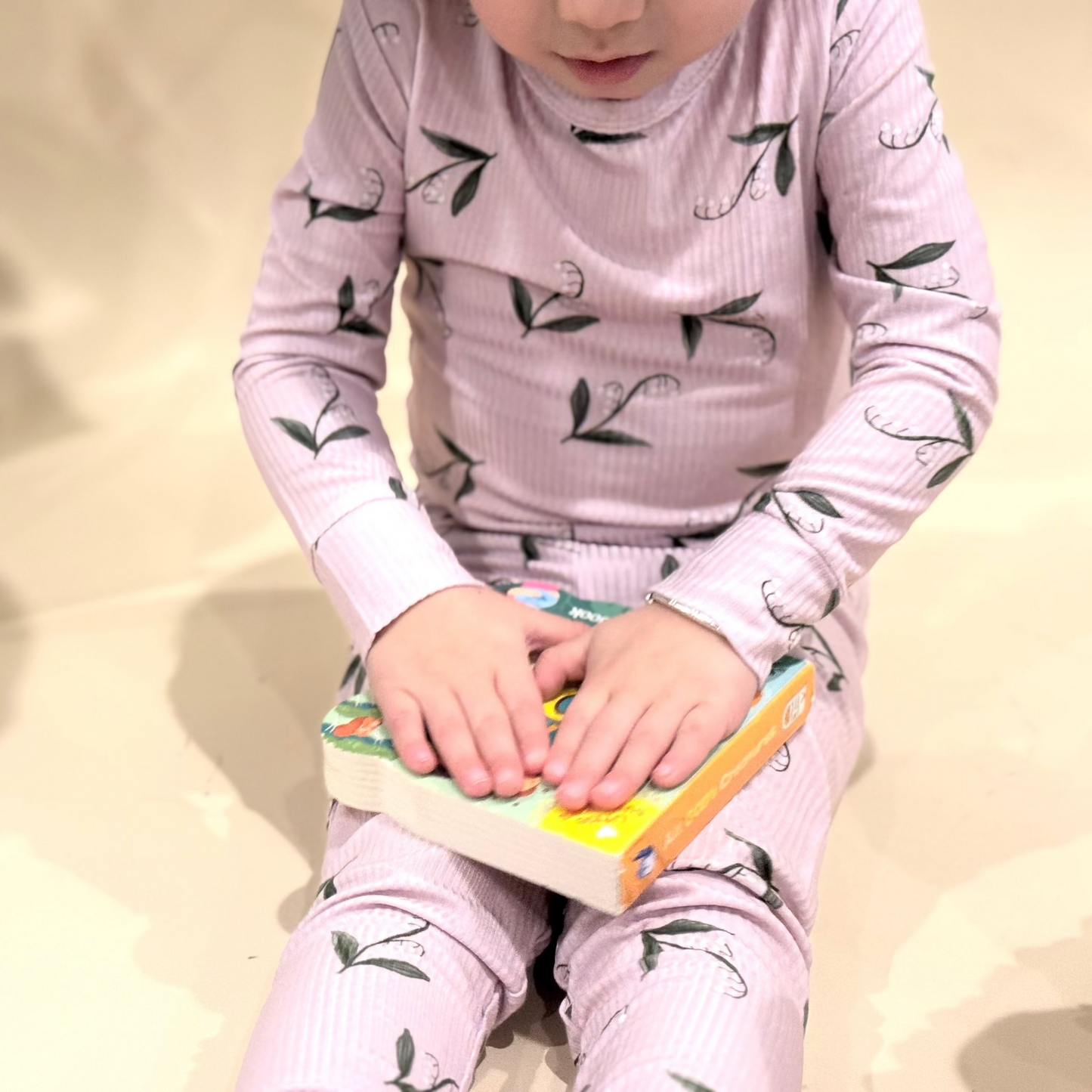 toddler in lily pattern PJs holding book