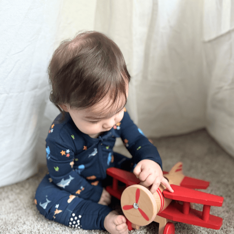 baby boy wearing sea animal pattern zip romper playing with wood airplane