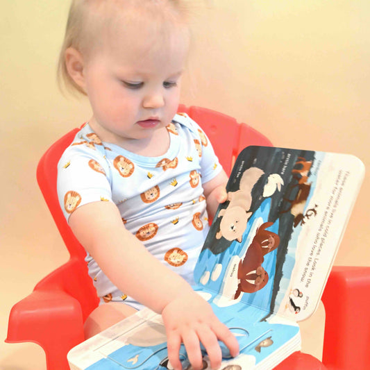 baby girl wearing lion and crown pattern onesie reading a book