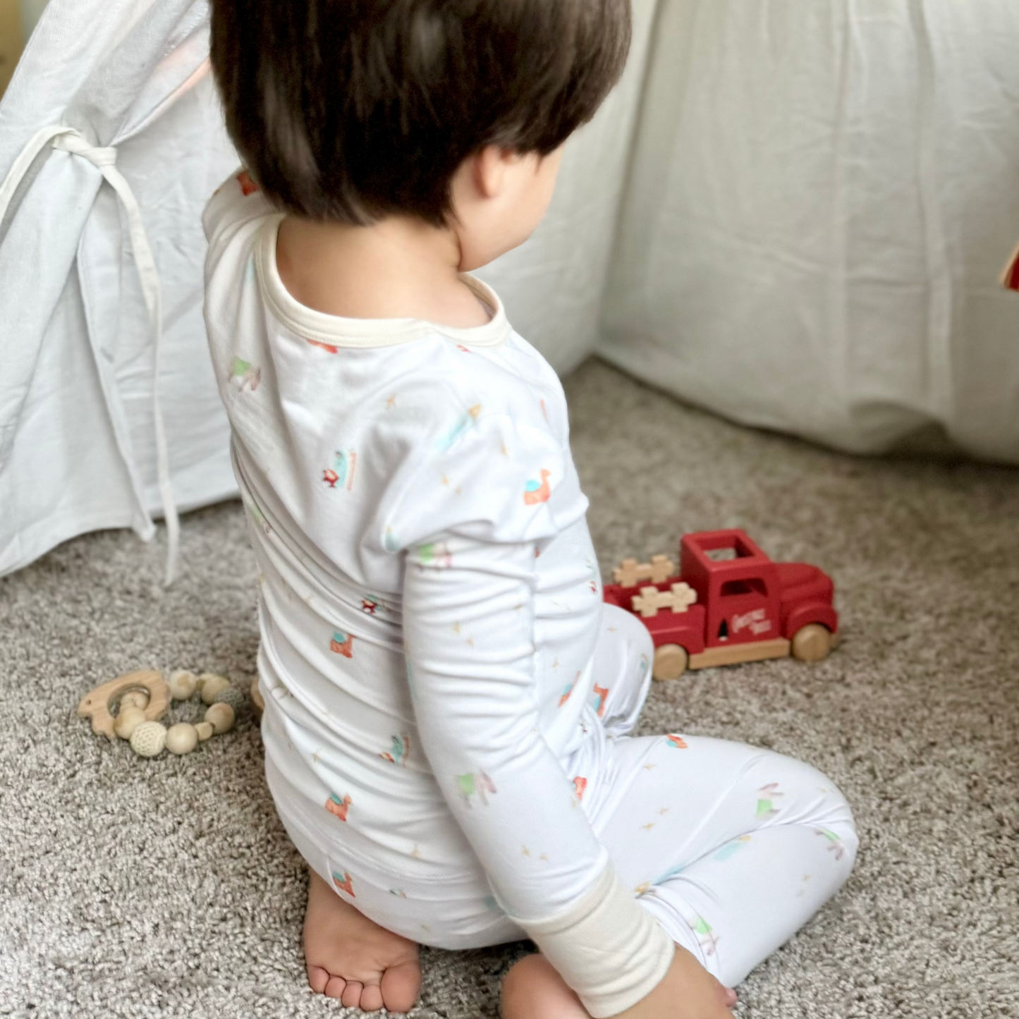 toddler boy in nativity pattern pajamas playing with wood Christmas toys