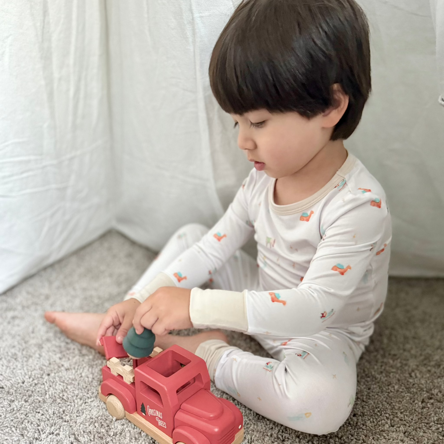 toddler boy in nativity pajamas playing with Christmas truck toy