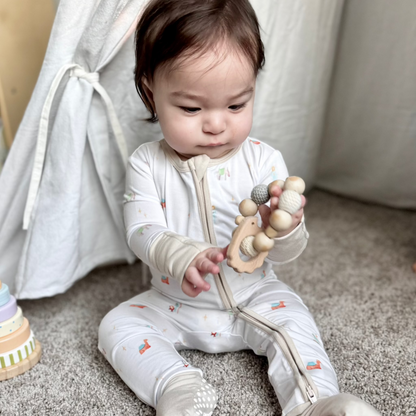 baby boy in nativity zip romper playing with wooden teether