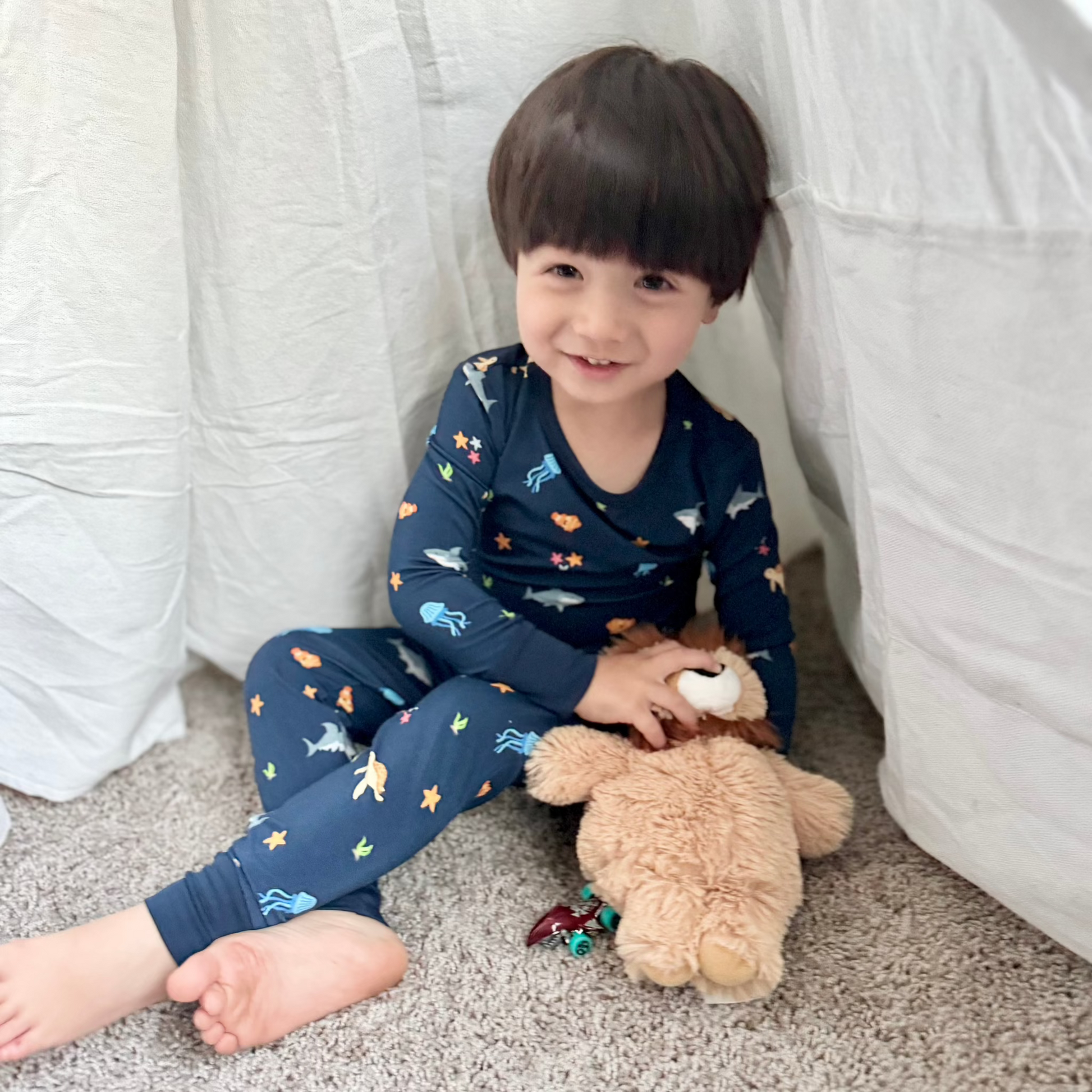 toddler boy in sea animal pajamas sitting with stuffed animal